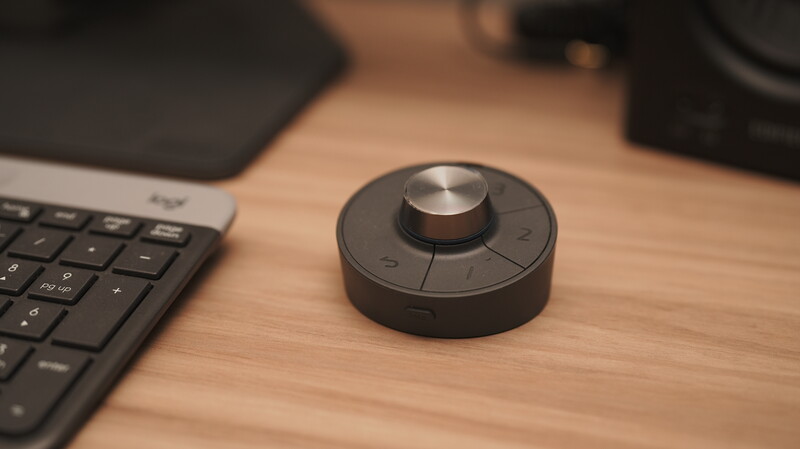 Black circular control device with metal knob and numbered buttons on wooden desk next to keyboard.