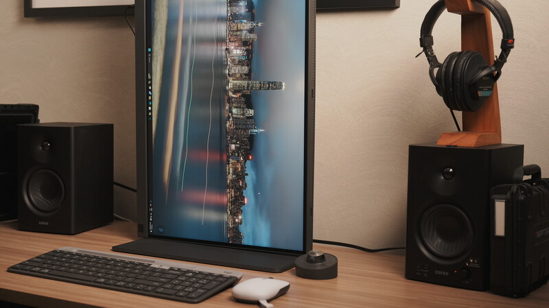 Creative workspace with monitor displaying cityscape, studio monitors, keyboard, mouse, and headphones on wooden desk.