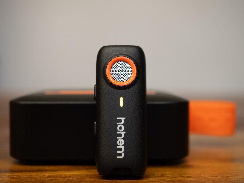 Black handheld device with orange circular lens element and white text on wooden surface next to black and orange rectangular objects.