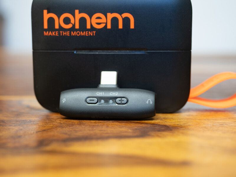Hohem smartphone gimbal stabilizer with orange charging cable on wooden surface.