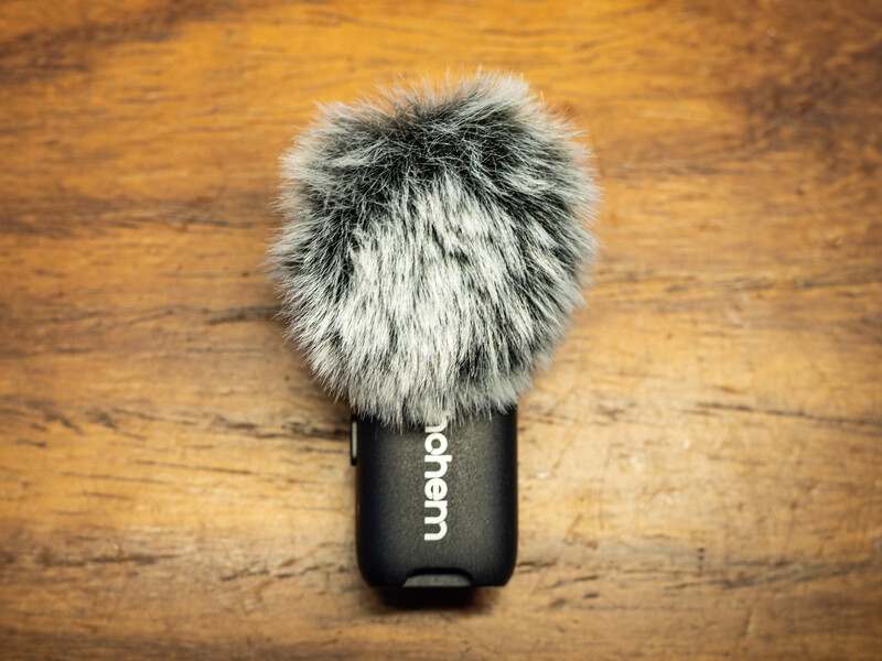 Rode microphone with fuzzy windscreen on wooden surface.