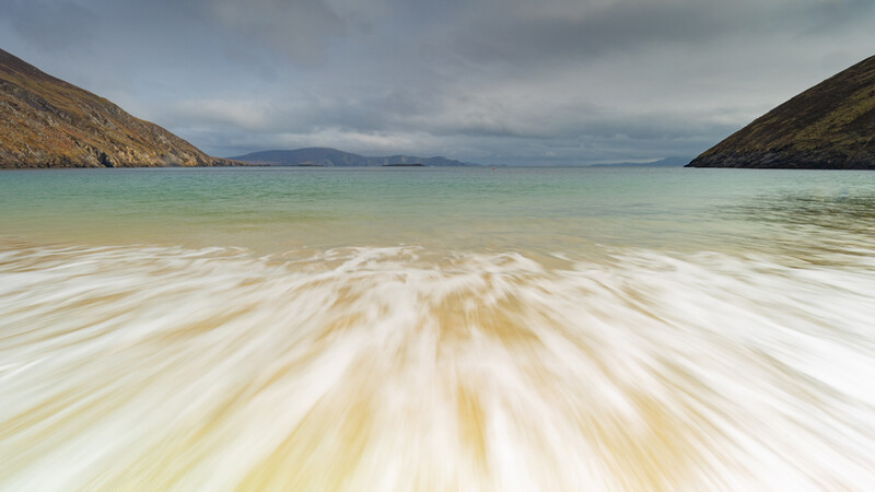 Long-exposure seascape with wave motion blur framed by rocky headlands and turquoise water.