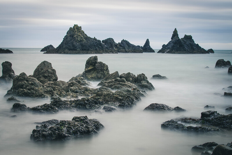 Misty seascape with jagged rock formations and distant sea stacks beneath overcast sky.