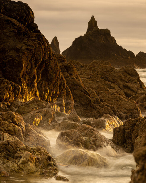 Dramatic coastal rock formations with golden hour lighting and flowing water motion blur.