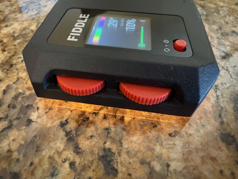 Portable lighting control device with digital display and dual red adjustment knobs on granite countertop.