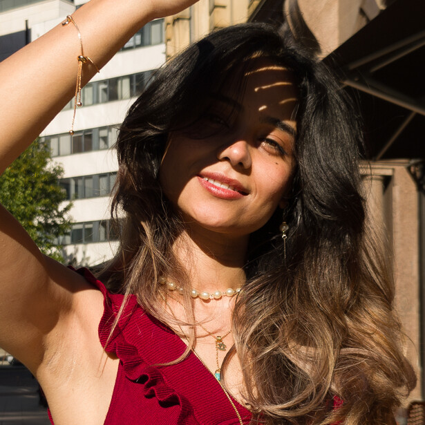 Woman in red top with long dark hair looking upward, backlit by warm sunlight creating shadow patterns across her face.