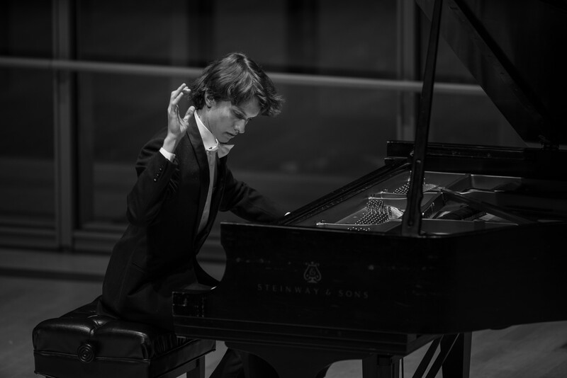 Pianist in formal attire performing at a grand piano in a black and white photograph.