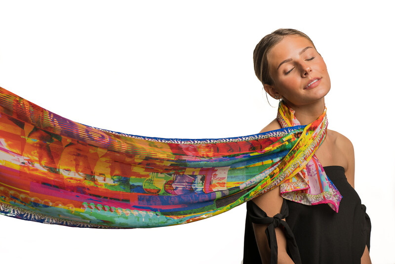 Woman with eyes closed wearing black off-shoulder top and vibrant rainbow patterned scarf flowing behind her head.