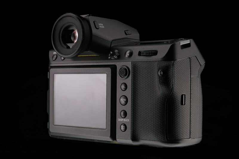 Medium format digital camera with articulating LCD screen and grip handle on black background.