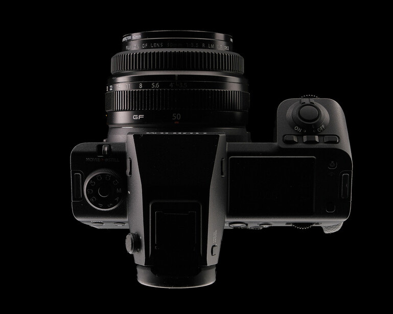 Top-down view of a vintage medium format camera with interchangeable lens and viewfinder components against black background.