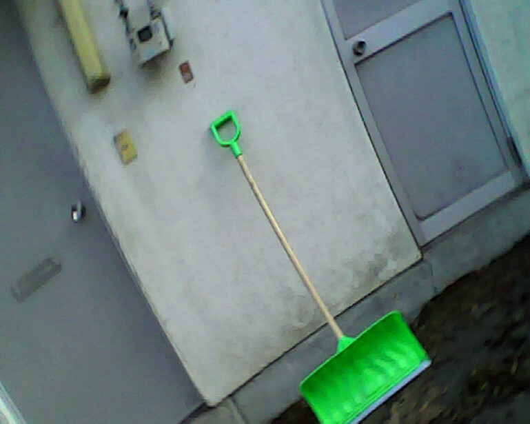 Green plastic shovel leaning against white appliance in indoor space.