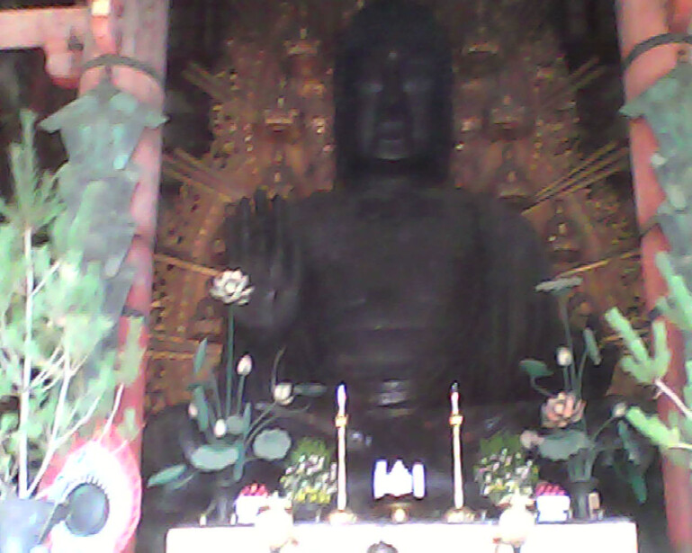 Large Buddha statue with ornate golden backdrop and lit candles on altar table.