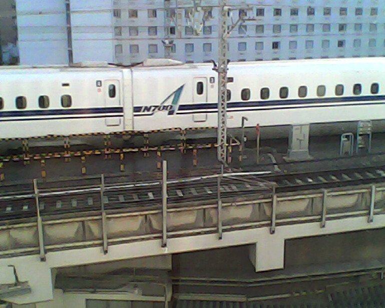 A white high-speed passenger train stopped at a platform station alongside residential buildings.