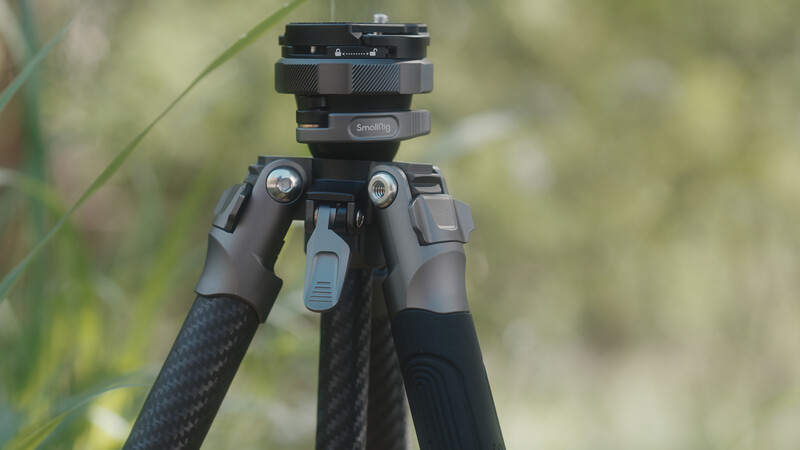 Carbon fiber tripod with ball head and blue quick-release lever against blurred green background.