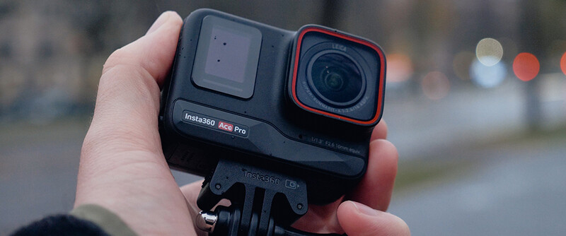 Insta360 Ace Pro action camera held in a hand, showing the dual-lens design with front display and red-accented main camera lens.