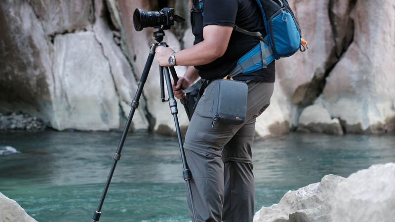 Photographer with camera on tripod positioned on rocky shore overlooking turquoise water and limestone cliffs.