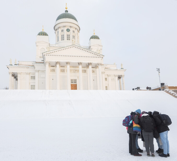 Group of people huddled together in deep snow facing a white neoclassical cathedral with green domes.