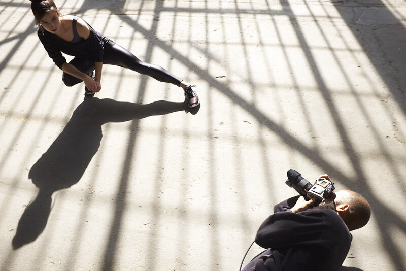 Overhead view of two people stretching on a concrete floor with geometric shadow patterns from window grilles.