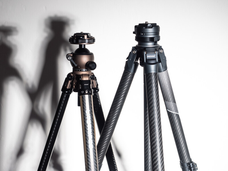 Two camera tripods with ball heads casting shadows against a white background.