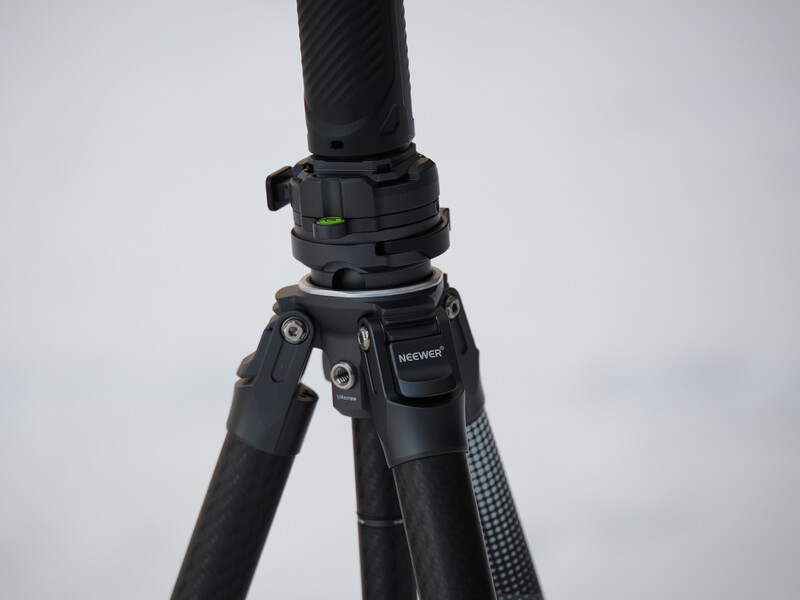 Close-up of a black camera tripod head with a bubble level and control knobs against a white sky.