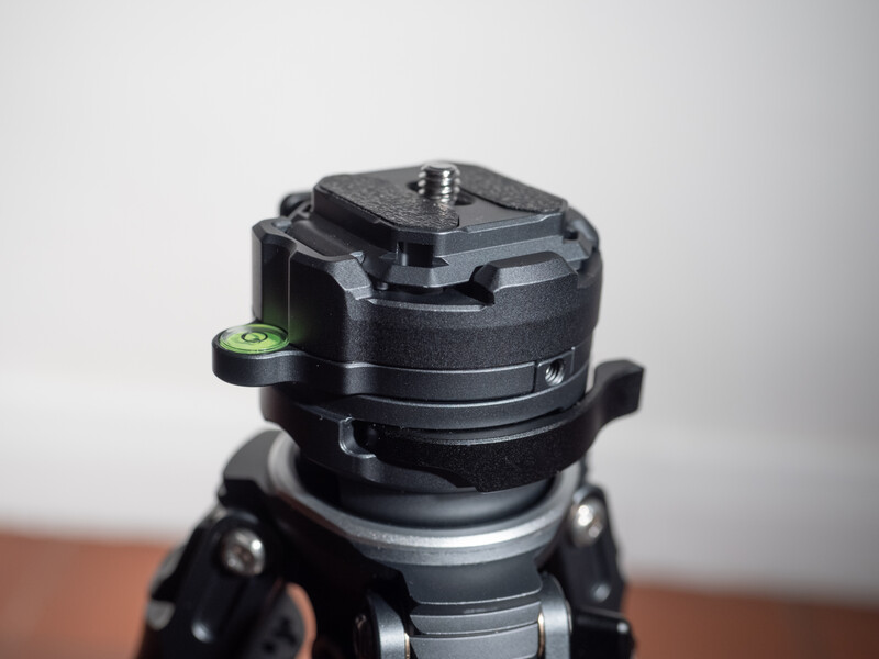 Black tripod head with mounted spirit level viewed from above against neutral background.
