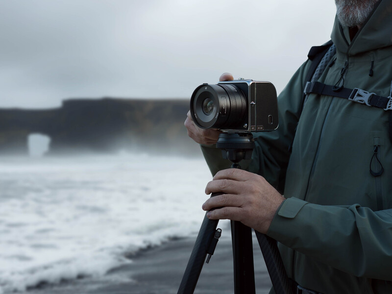 Photographer holding a camera on a tripod while facing a stormy seascape with crashing waves.