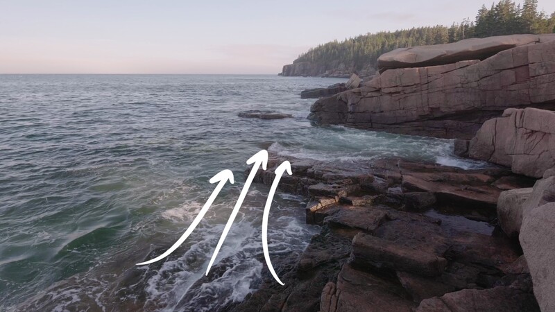 Rocky coastline with three white arrows overlaid on waves, indicating directional water movement or compositional flow.