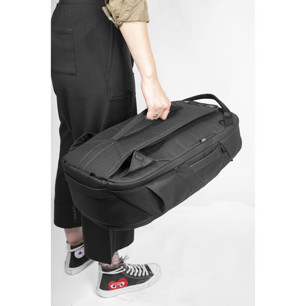 Person holding a black camera bag with multiple compartments and handles against their torso.