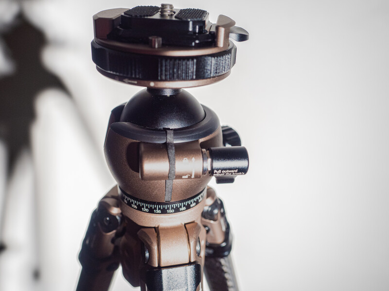 Ball head tripod mount with friction controls and quick-release plate against white background.