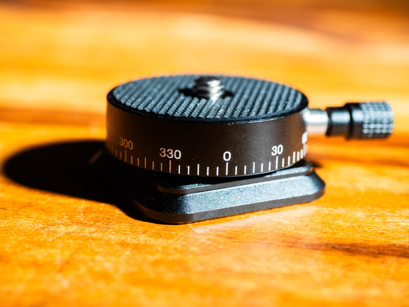 Black panoramic tripod head with degree markings and adjustment knob on warm wooden surface.