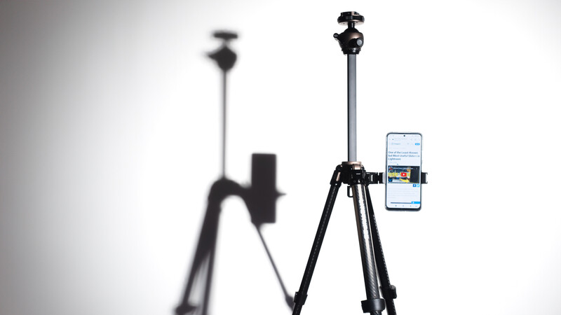 Smartphone mounted on a tripod with ball head, shown in sharp focus alongside a blurred tripod in the background.