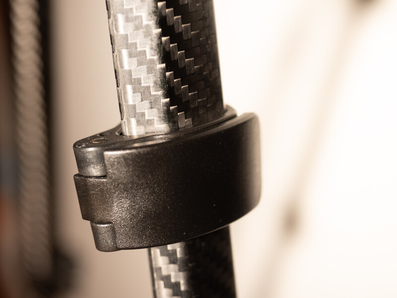Black cable management clamp securing a carbon fiber tube against a blurred background.