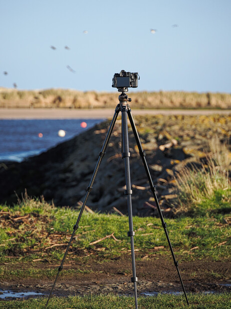 Camera mounted on tripod in agricultural field with water and distant landscape.