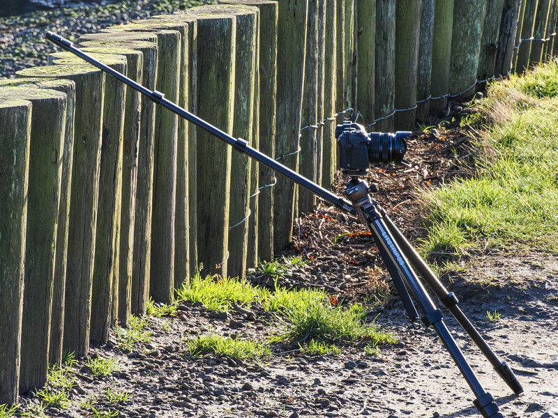 Mountain bike leaning against weathered wooden fence posts alongside a gravel path with grass edges.