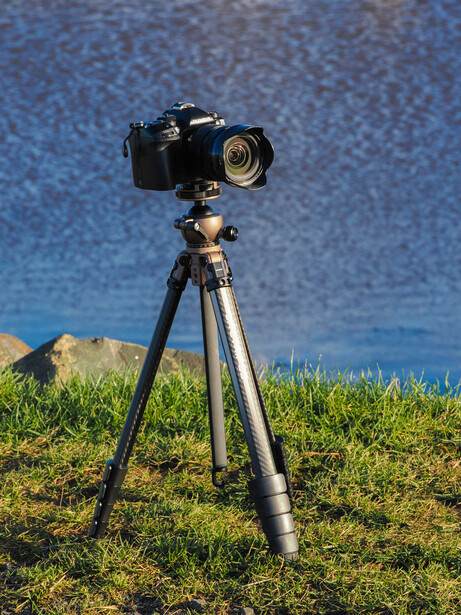 DSLR camera mounted on tripod overlooking calm blue water and green grass.