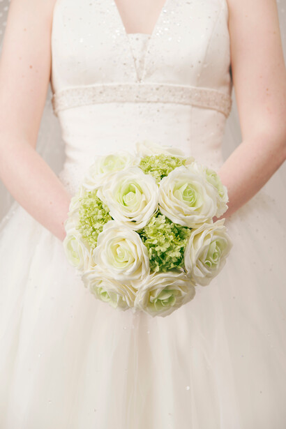 Bride in white wedding dress holding a bouquet of cream roses and green hydrangeas.