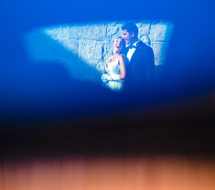 Couple in formal attire illuminated by blue and warm orange gradient lighting against a textured backdrop.