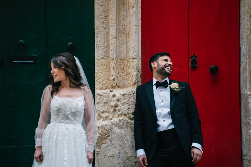 Bride and groom standing against contrasting green and red doors during formal portrait session.