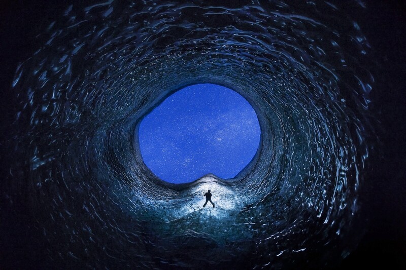 Silhouetted figure standing in a dark tunnel opening toward bright blue sky.