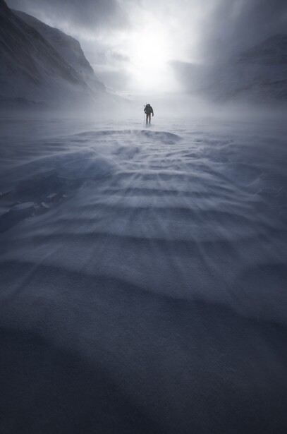 Solitary figure standing on a vast, rippled water surface beneath dramatic cloudy sky with bright light breaking through.