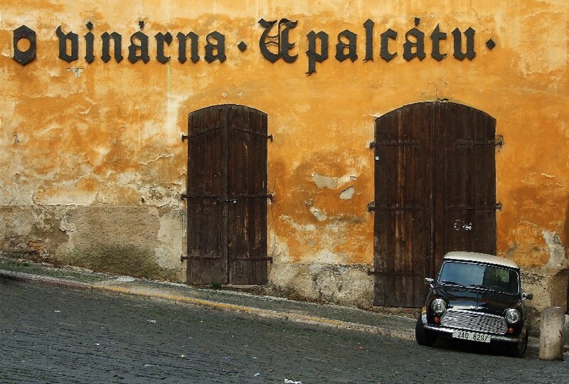 Weathered yellow ochre wall with two dark wooden doors and a vintage car parked in front.