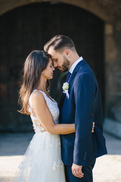 Bride and groom sharing an intimate moment during their first kiss, with soft natural lighting and blurred architectural background.