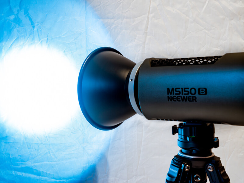 Neewer monolight mounted on tripod producing bright blue-white flash against textured backdrop.
