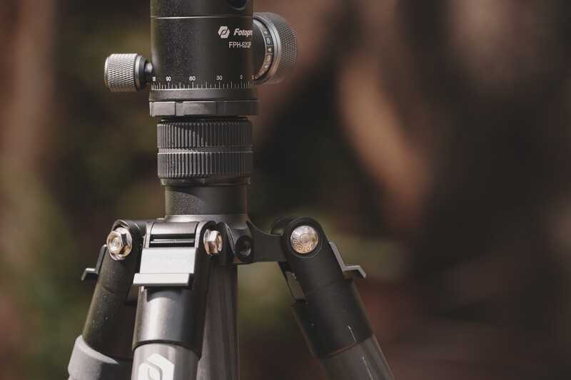 Tripod head with leveling base mounted on carbon fiber legs with blurred background.