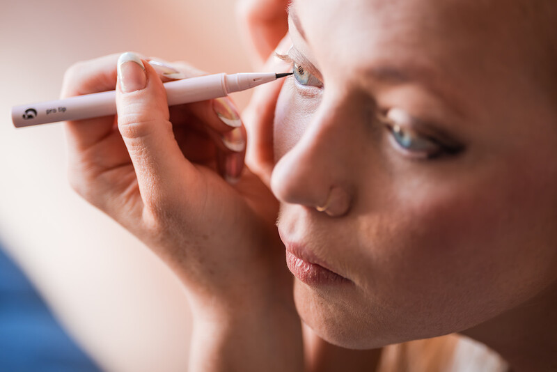 Woman applying makeup with a brush near her eye in close-up portrait.