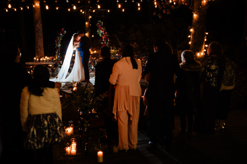Nighttime outdoor wedding ceremony with couple exchanging vows under string lights and decorated arch.