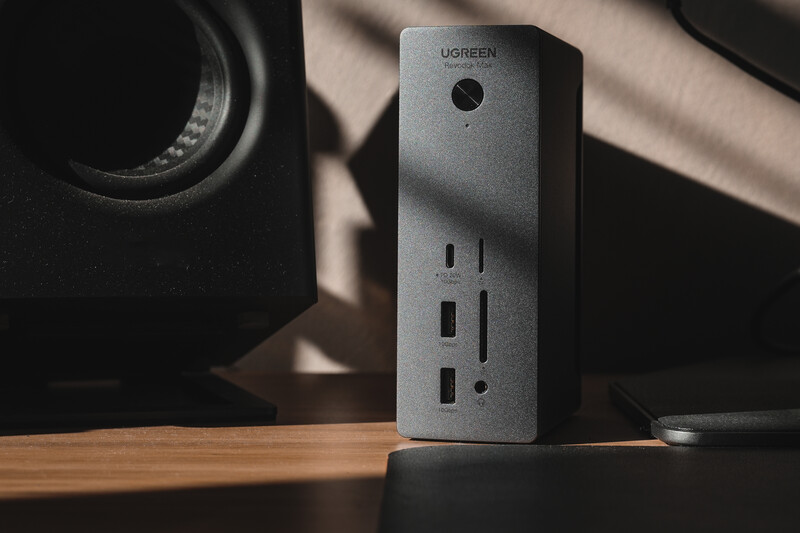 Ugreen power strip with multiple outlets displayed on wooden desk beside speakers in studio lighting.