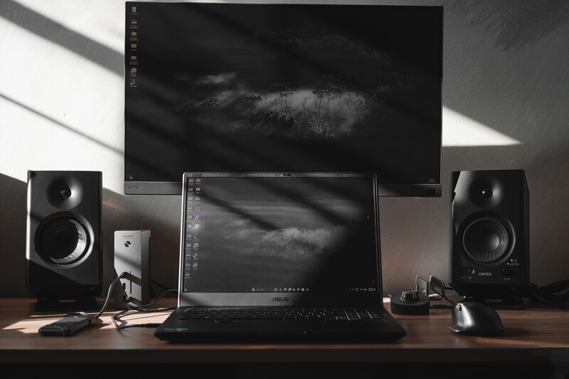 Professional photo editing workspace with dual monitors displaying dark landscape images, flanked by studio speakers and peripheral devices.