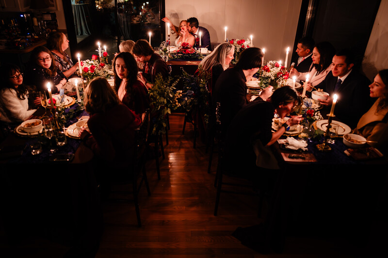 Candlelit dinner event with guests seated at long tables in an elegant indoor venue.