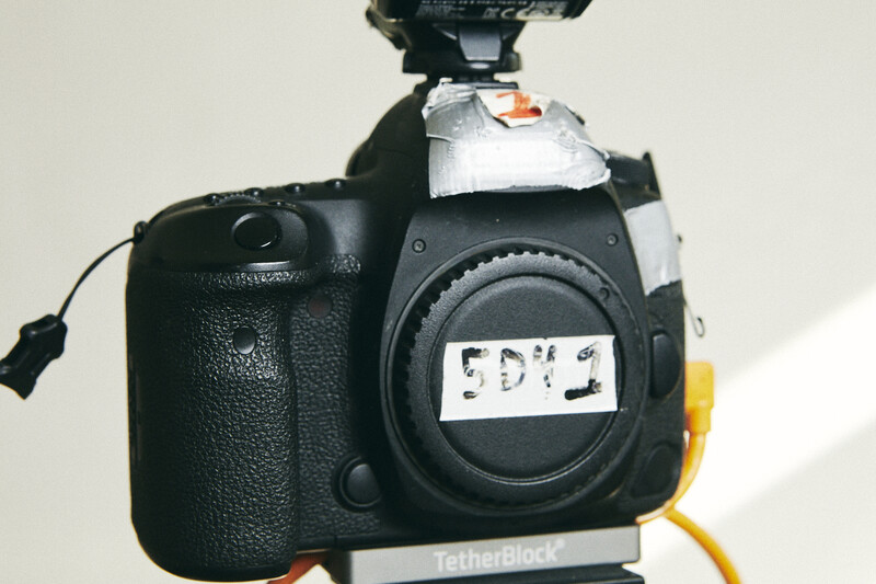 Canon DSLR camera body with flash mounted on top, positioned against white background with studio lighting.